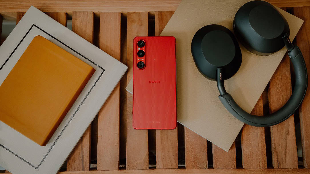 A red cell phone and headphones on a wooden surface Description automatically generated